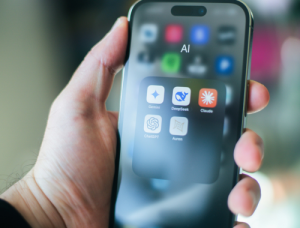 Une main tient un smartphone dont le dossier « AI » regroupe les applications Gemini, DeepSeek, Claude et ChatGPT.